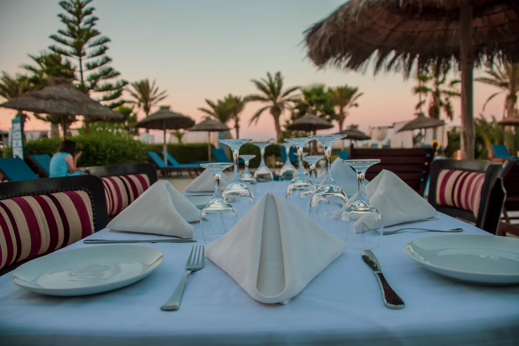 Table dressée pour le dîner sur la plage de Dar El Bhar au coucher du soleil, serviettes pliées en éventail