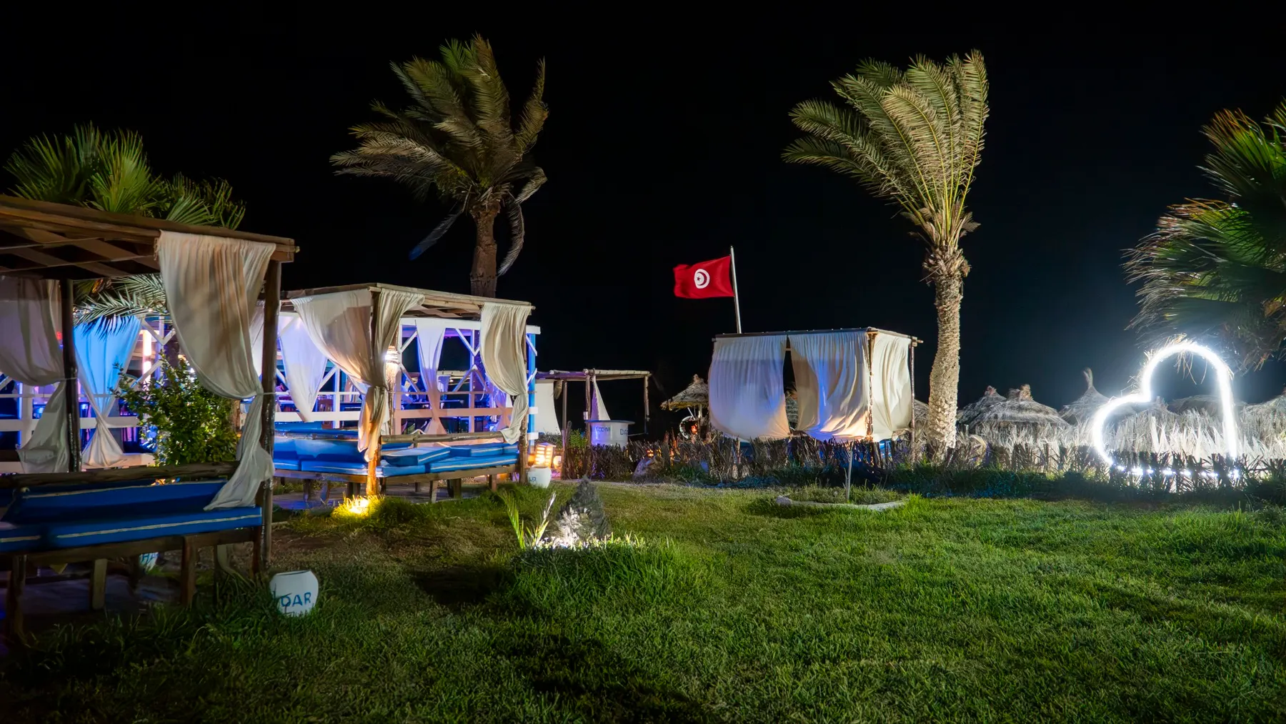 Les cabanes du beach bar de Dar El Bhar éclairées à la nuit tombée, sous les palmiers