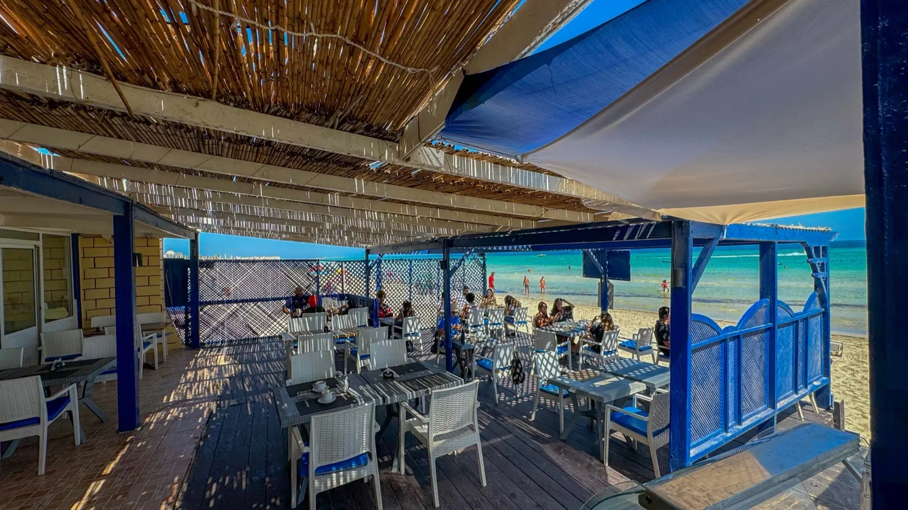 Tables dressées dans le sable sous la pergola du beach bar de Dar El Bhar